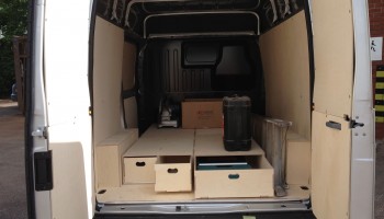 Back of a van with doors open showing floor drawers, two of which are open